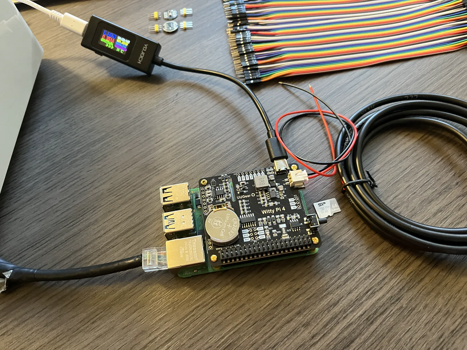 The Witty Pi 4 seated on the Raspberry Pi, the row of 40 pins along its edge, the coin battery in its holder, the meter's cable in the Witty Pi's USB-C socket
