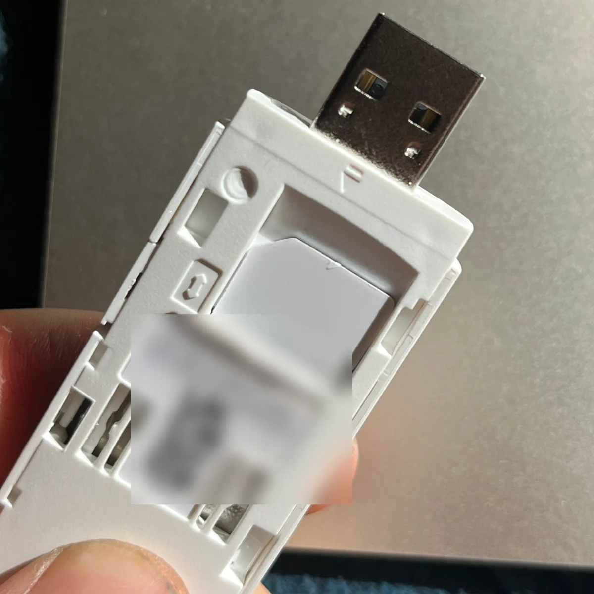 The opened 4G stick held with its USB plug pointing up: the SIM lies in its slot with the blank side up and its cut corner at the top right, next to a small corner mark in the plastic